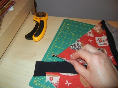 Overlap the triangles over another black strip. My strips are about 2 inches wide.  The triangle overlaps it about 1/2 inch.  The process of sewing the original squares and strips together to make the 'banner' is similar to this.